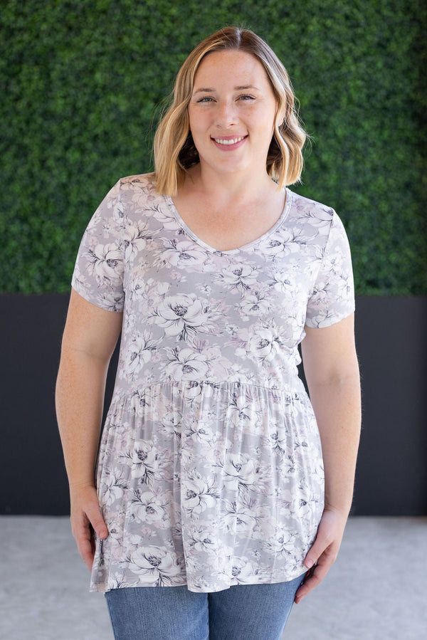 Woman wearing a floral blouse standing against a green hedge background