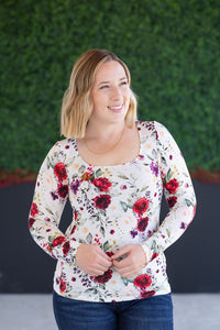 Woman wearing a floral long-sleeve top against a green hedge background
