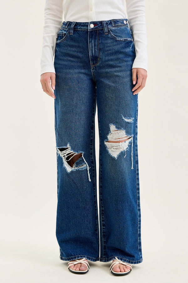 Person wearing blue distressed wide-leg jeans on a white background