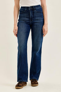 A model wearing a pair of dark blue high-rise flare jeans, paired with leopard print shoes and a white ribbed top, photographed against a solid light beige background.