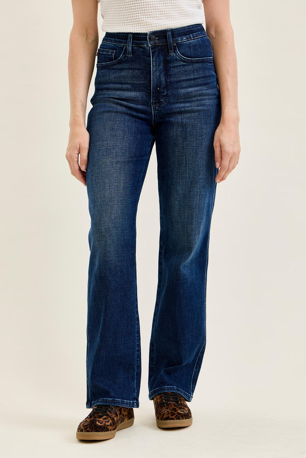 A model wearing a pair of dark blue high-rise flare jeans, paired with leopard print shoes and a white ribbed top, photographed against a solid light beige background.