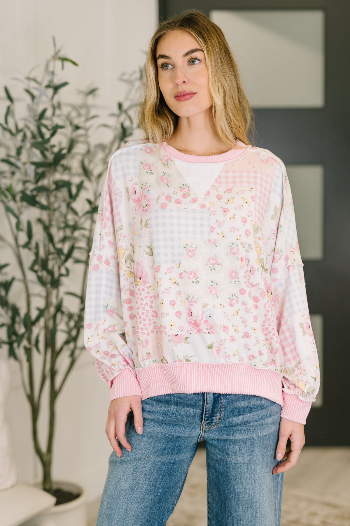 Woman wearing a floral blouse with a pink trim and blue jeans indoors.