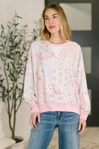 Woman wearing a floral blouse with a pink trim and blue jeans indoors.