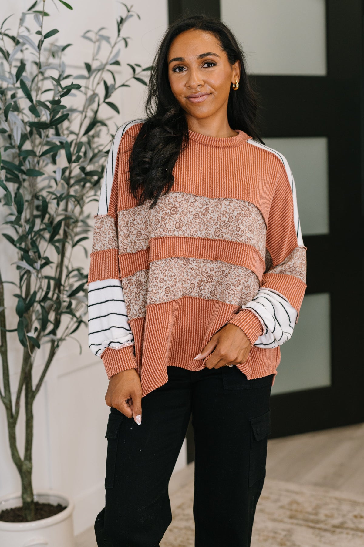 Woman wearing a patterned sweater standing indoors with a plant in the background