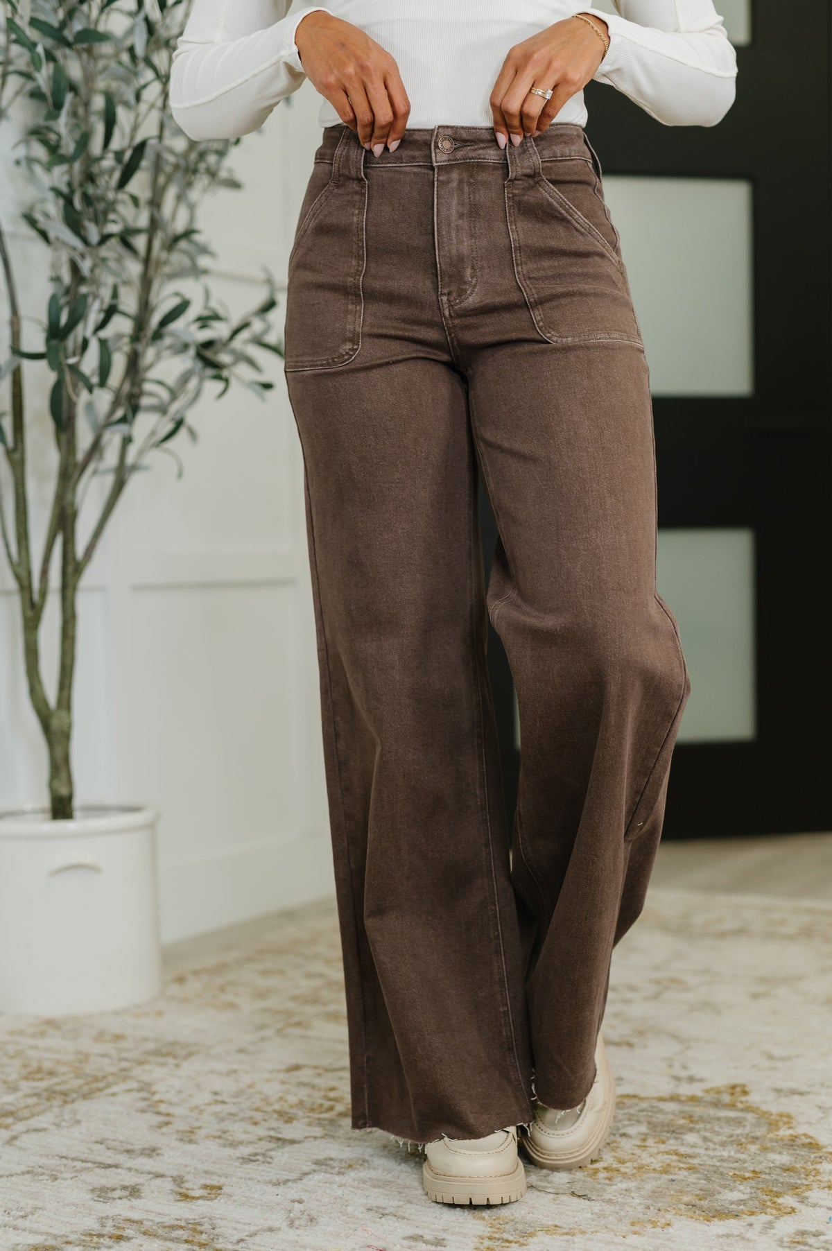 Person wearing brown wide-leg pants and a white shirt indoors.