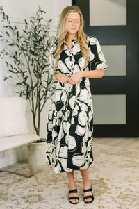 Woman wearing a black and white patterned dress in a room with a plant and bench.