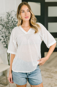 Woman wearing a white textured top and denim shorts indoors.