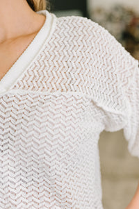 Close-up of a person wearing a textured white sweater with a blurred background