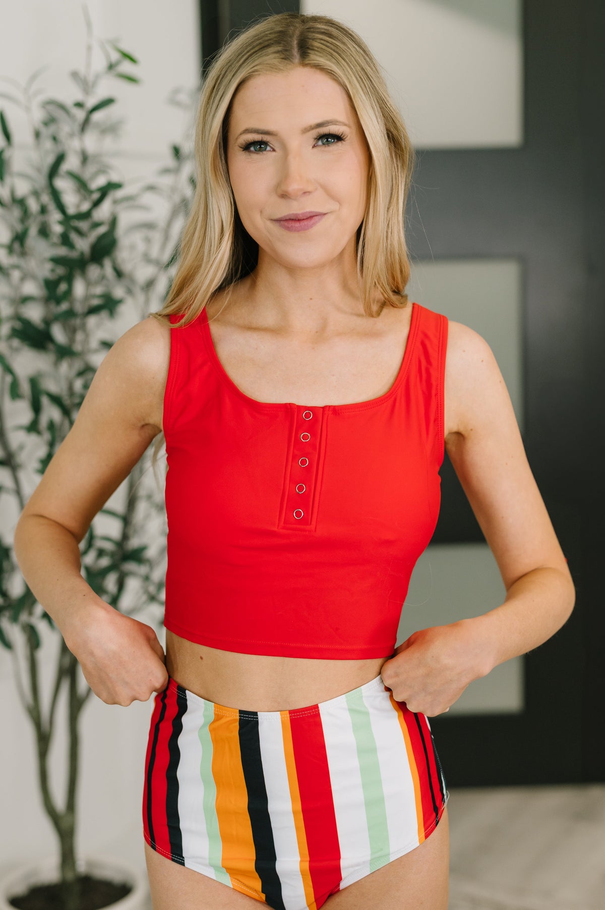Woman wearing a red top and colorful striped shorts indoors.