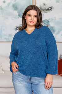 Woman wearing a blue sweater and jeans in a room with a blurred background