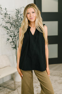 A woman modeling a sleeveless black V-neck top with olive green wide-leg pants in a modern indoor setting.