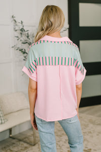 Person wearing a pink and green striped shirt in a room with a couch and plant.