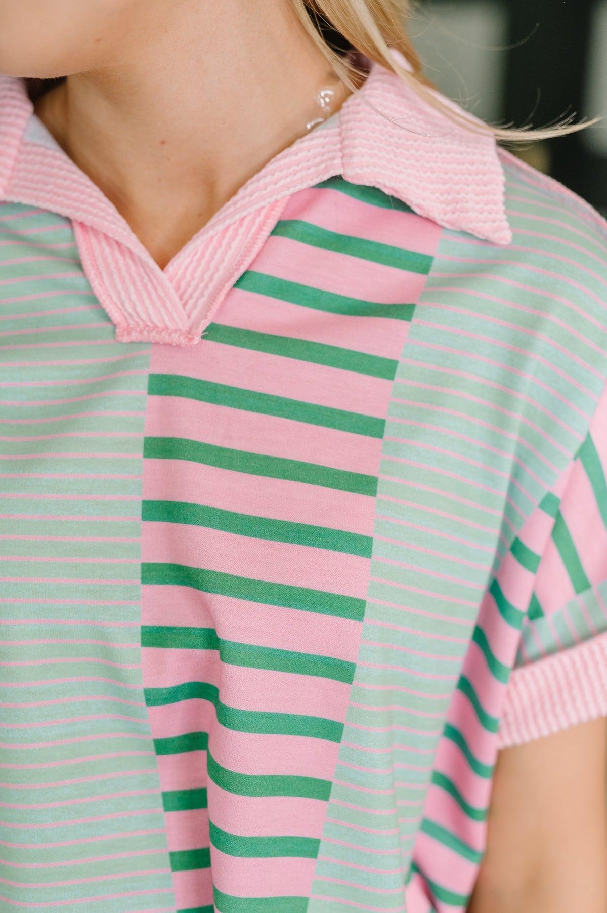 Close-up of a person wearing a pink and green striped polo shirt.