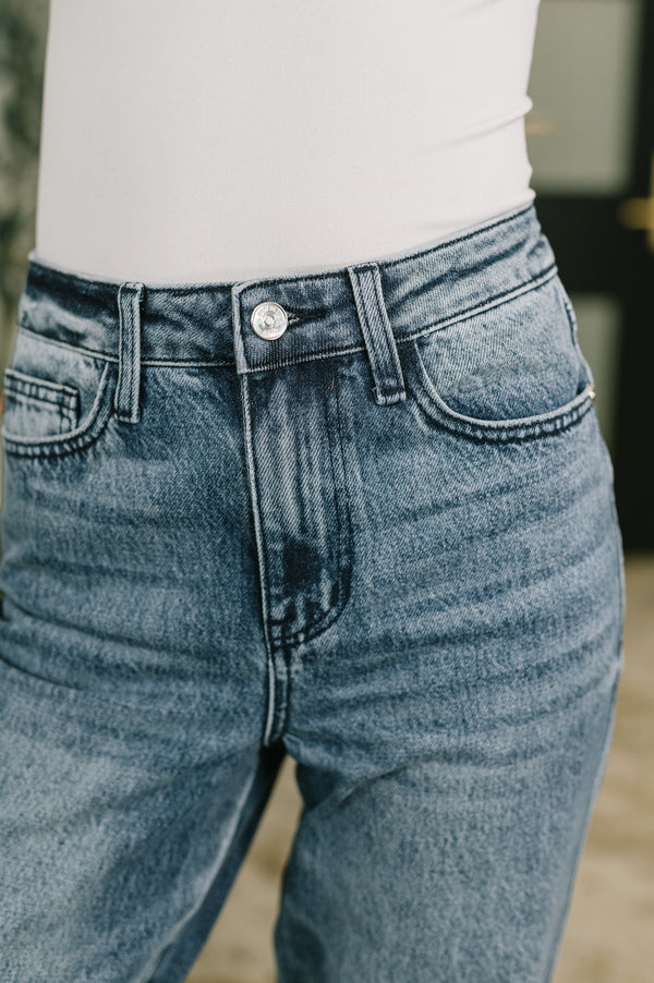 Close-up of a person wearing light blue denim jeans with a white top, showing the waistband, button, belt loops, front pockets, and upper legs.