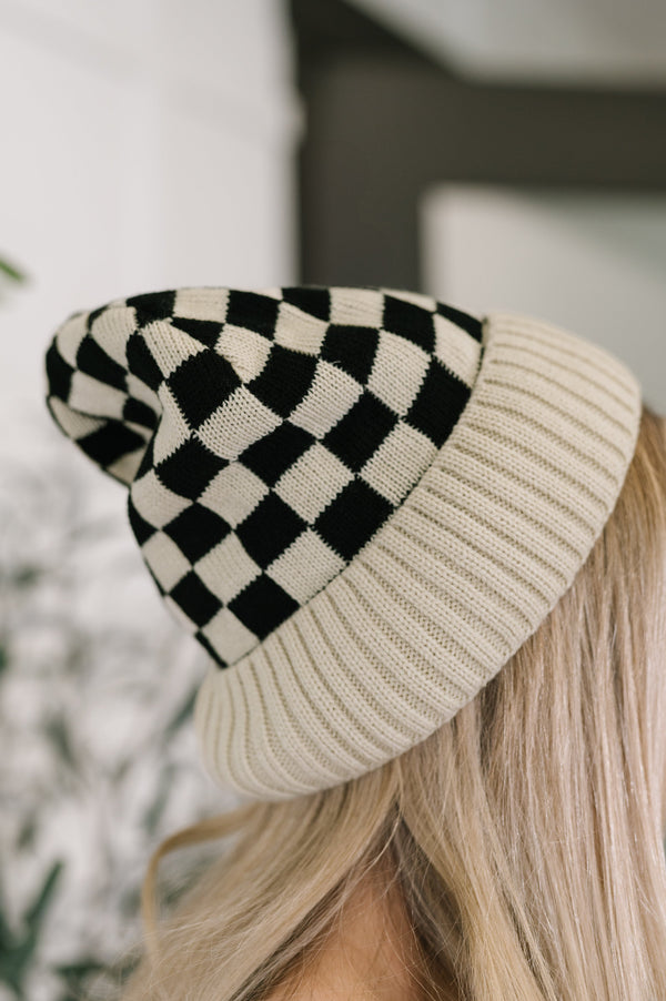 Checkered beanie with beige and black pattern worn by a person with blonde hair.