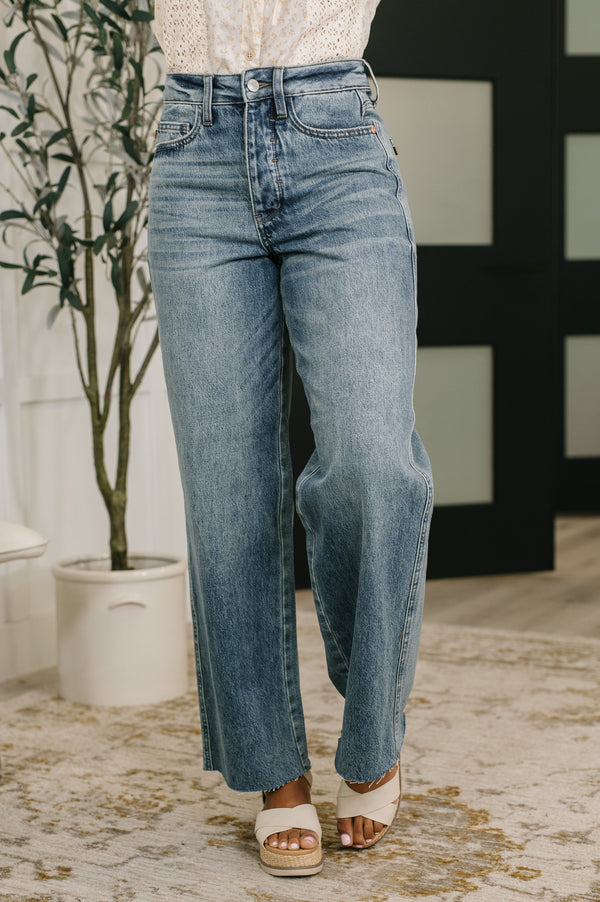 Person wearing blue jeans standing indoors with a plant and decorative wall in the background