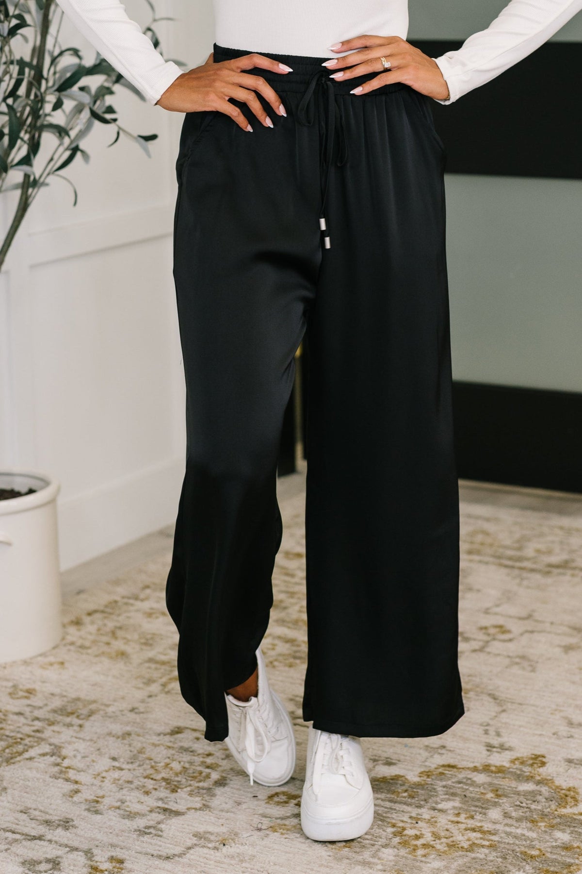 Person wearing black wide-leg pants and white sneakers indoors.