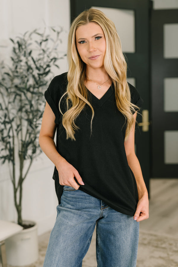 Woman wearing a black sleeveless top and blue jeans indoors.