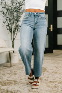 Person wearing light blue jeans and white sandals in an outdoor setting.