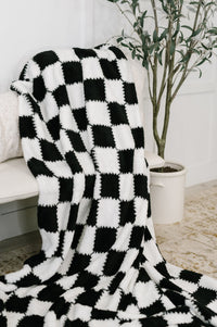 Black and white checkered blanket draped over a chair with a plant in the background.