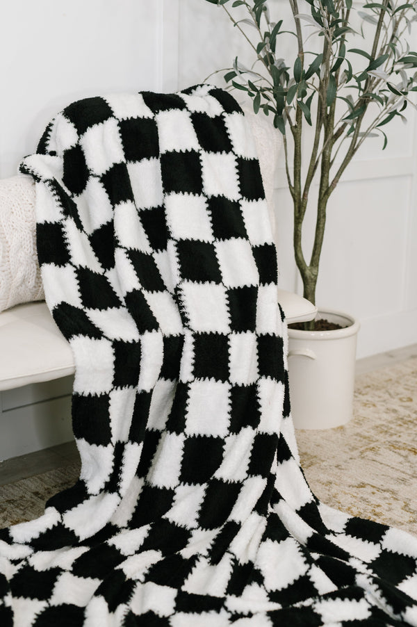 Black and white checkered blanket draped over a chair with a plant in the background.