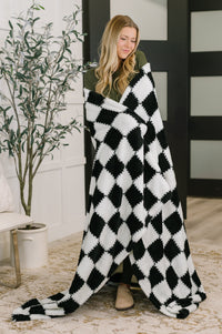 Woman wrapped in a black and white checkered blanket in a room with a plant and furniture.