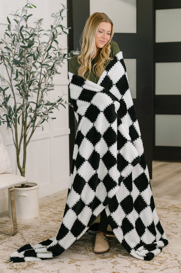 Woman wrapped in a black and white checkered blanket in a room with a plant and furniture.