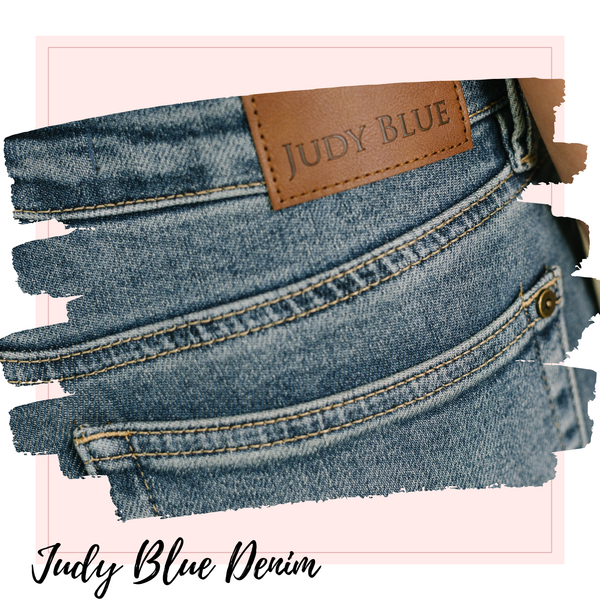 Close-up of blue denim jeans showing the back pocket, stitching, a brown leather patch with 'JUDY BLUE' text, and the words 'Judy Blue Denim' at the bottom on a pink graphic background.