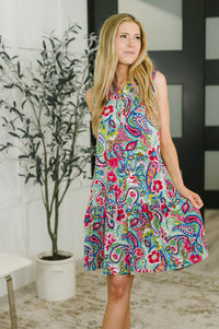 Woman wearing a colorful paisley dress in an indoor setting with a plant in the background.