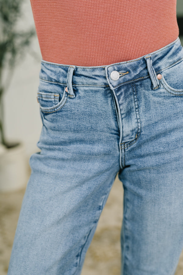 Close-up of a person wearing light-wash blue denim jeans and a textured coral-pink ribbed top, cropped from the waist down.