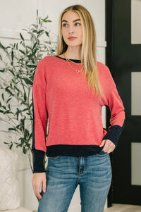 Woman wearing a red sweater with black cuffs and trim, standing indoors.