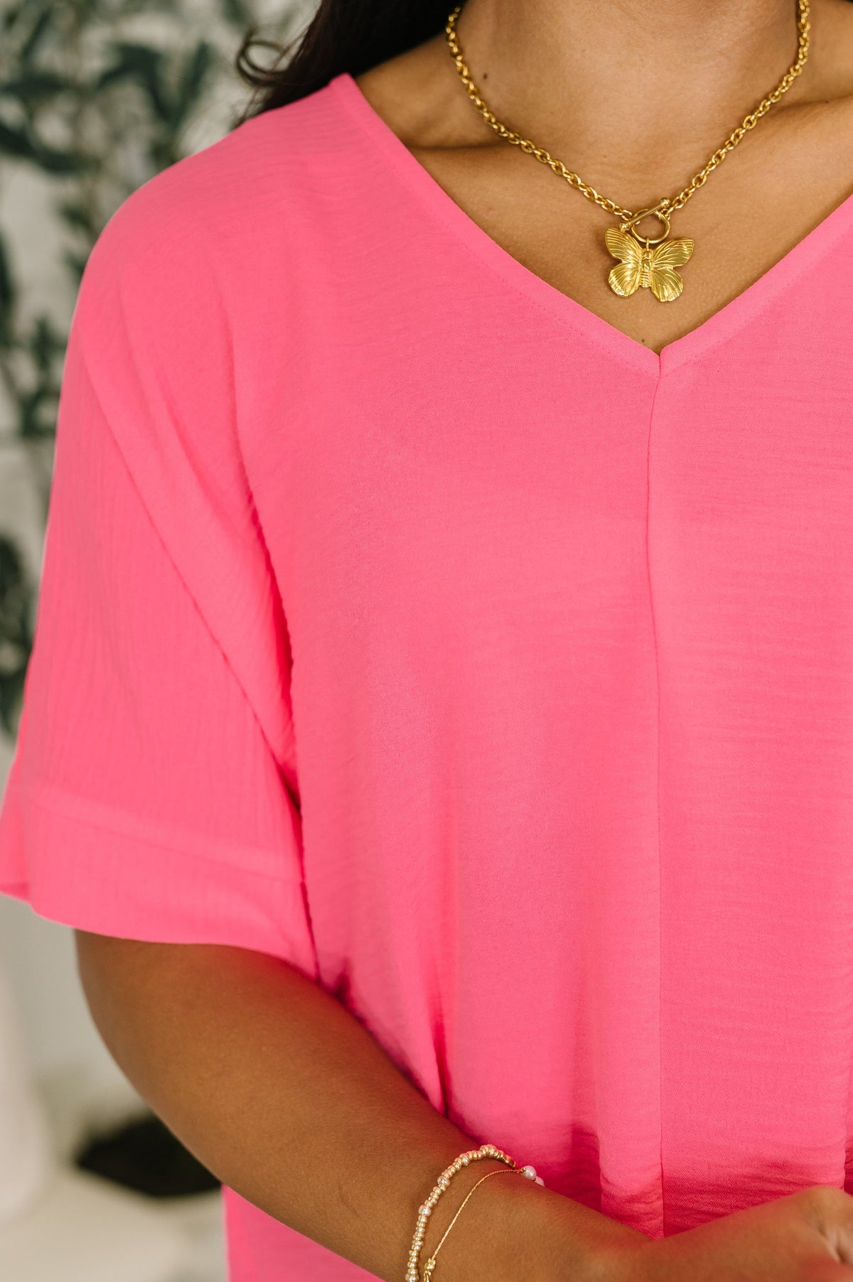 Person wearing a bright pink top and gold necklace with a pendant.