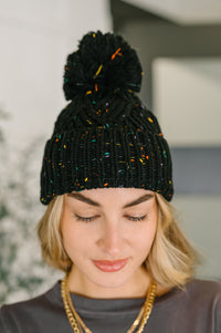 Person wearing a black knit beanie with colorful accents indoors