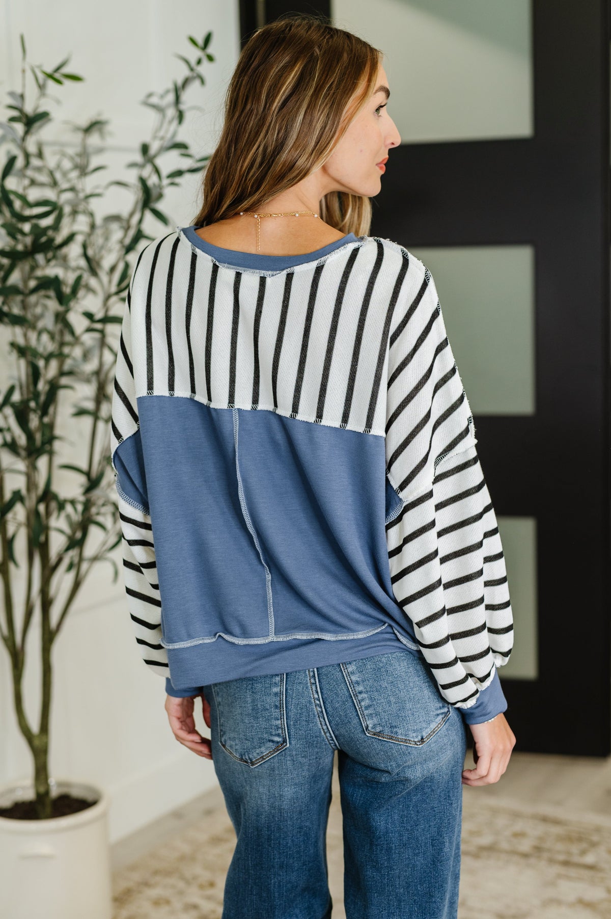 Woman wearing a striped sweater and jeans standing indoors with a plant in the background