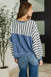 Woman wearing a striped sweater and jeans standing indoors with a plant in the background