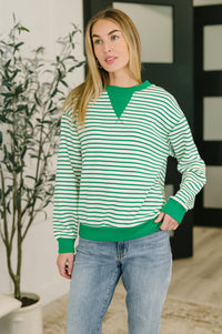 Woman wearing a green and white striped sweater with blue jeans indoors.
