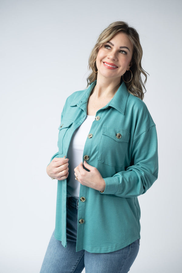 Woman wearing a teal jacket over a white shirt on a white background
