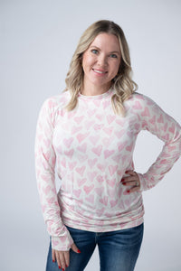 Woman wearing a white long-sleeve shirt with pink heart patterns on a plain background