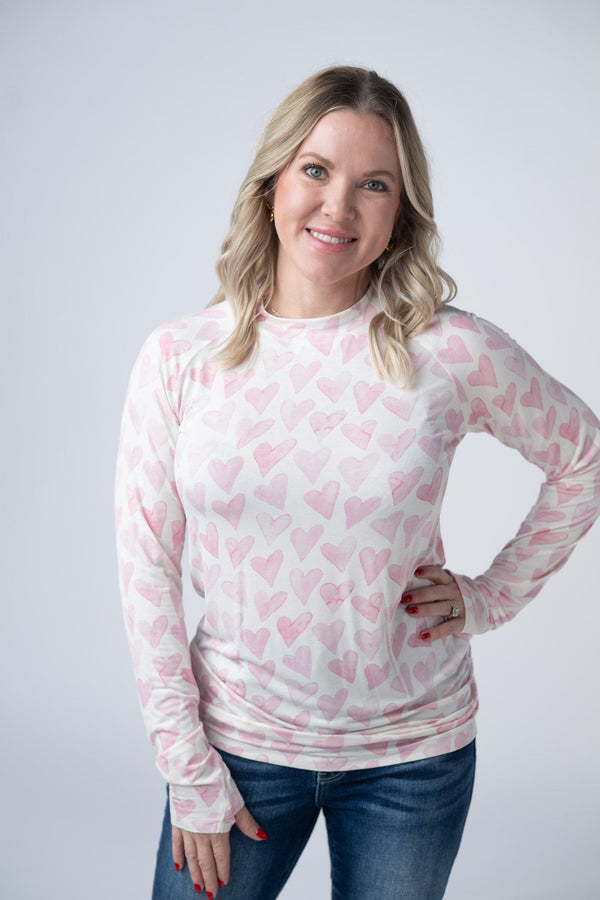 Woman wearing a white long-sleeve shirt with pink heart patterns on a plain background