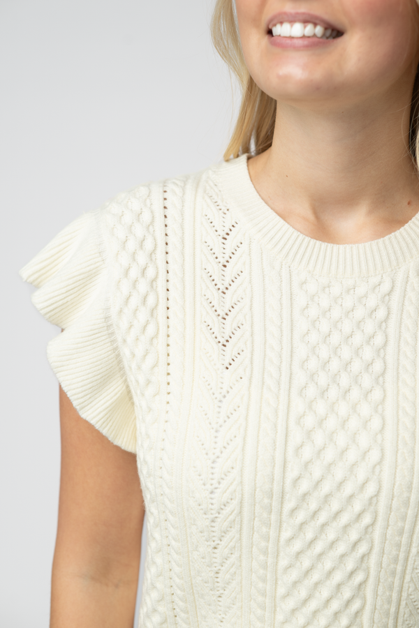 Woman wearing a cream-colored knit sweater with ruffled sleeves against a plain background