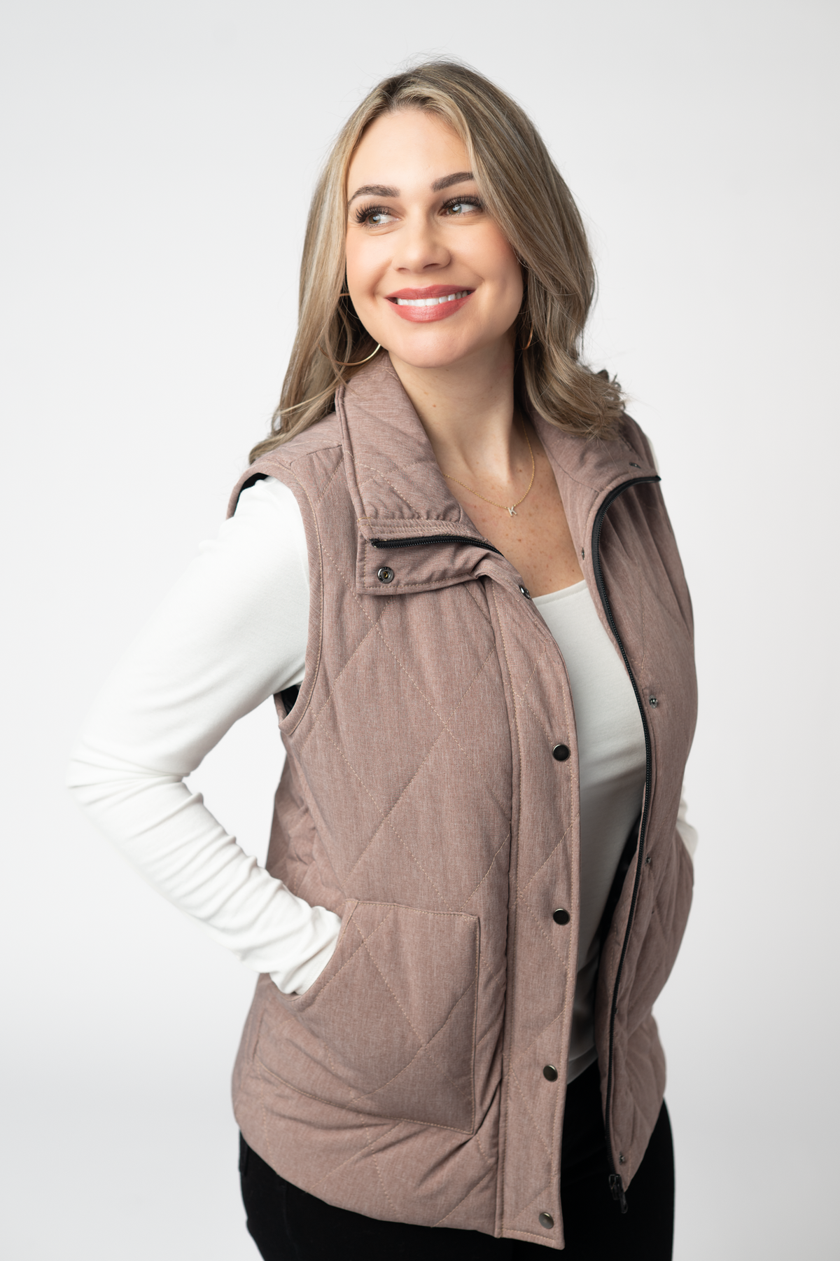 Woman wearing a quilted vest over a white long-sleeve shirt on a white background