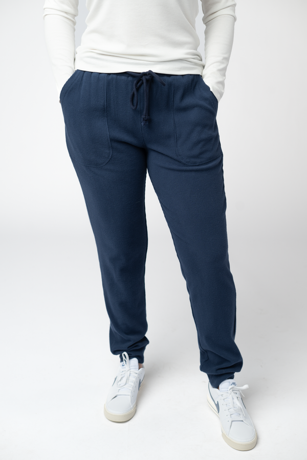 Person wearing navy jogger pants and white sneakers on a white background