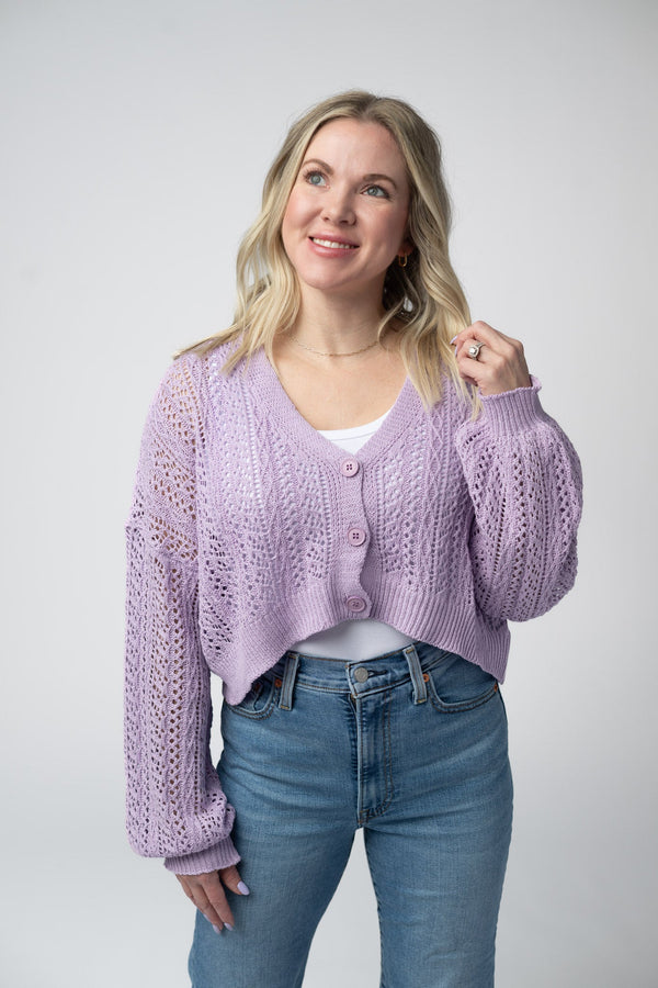 Woman wearing a light purple cardigan and blue jeans on a plain background