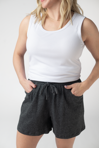 Person wearing a white tank top and dark gray shorts on a plain background