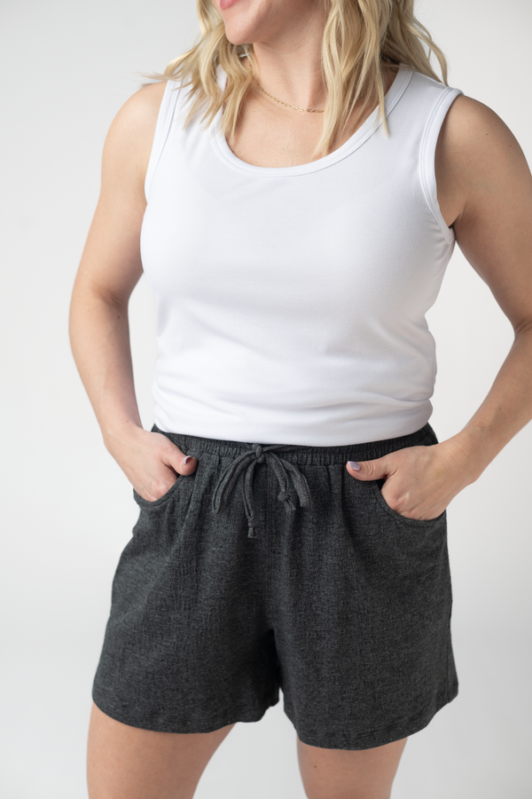Person wearing a white tank top and dark gray shorts on a plain background