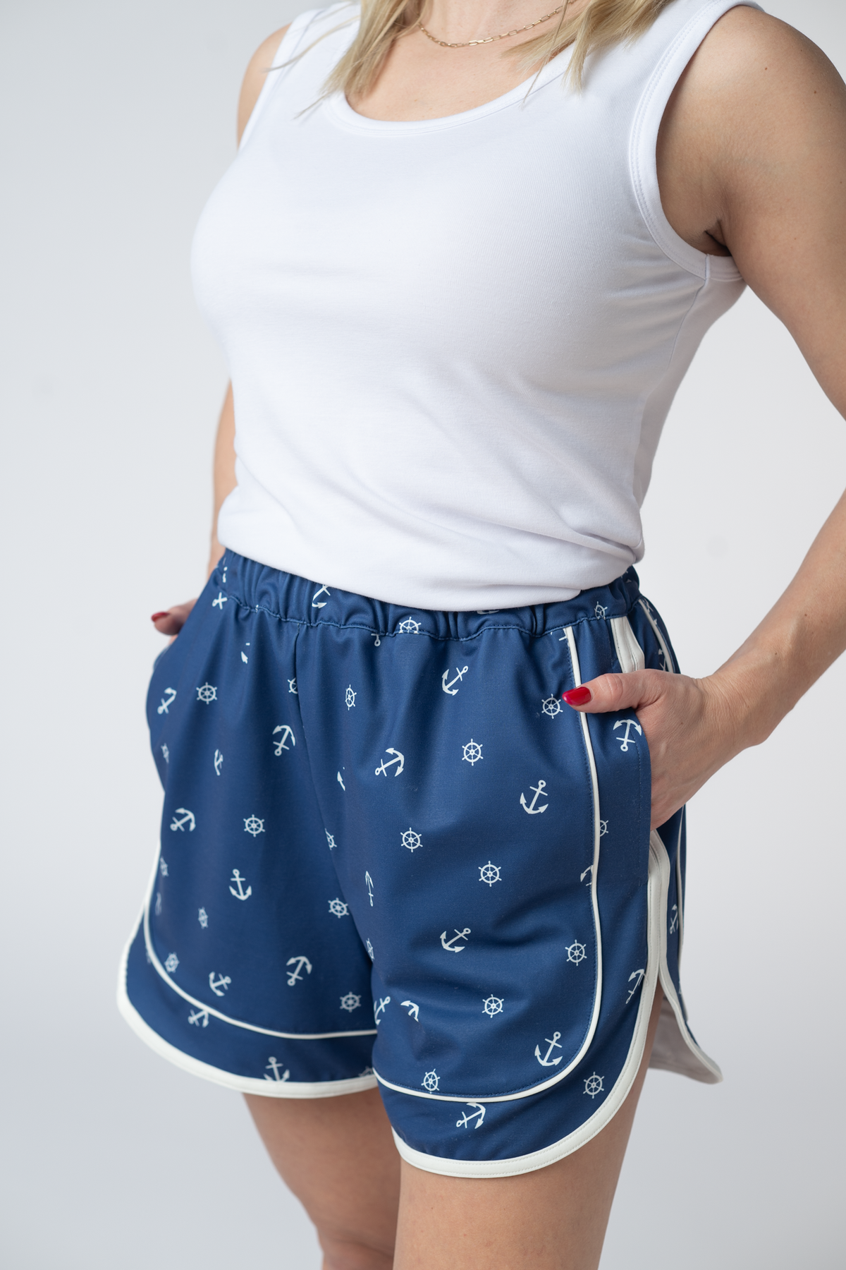 Person wearing blue shorts with anchor pattern and white tank top on gray background