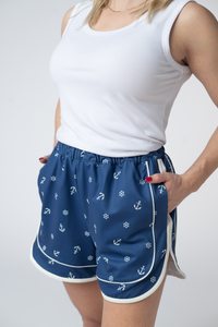 Person wearing blue shorts with anchor pattern and white tank top on gray background