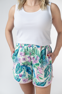 Person wearing a white tank top and tropical print shorts on a plain background
