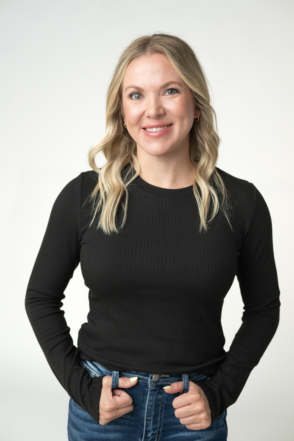 Woman wearing a black long-sleeve top and blue jeans against a white background