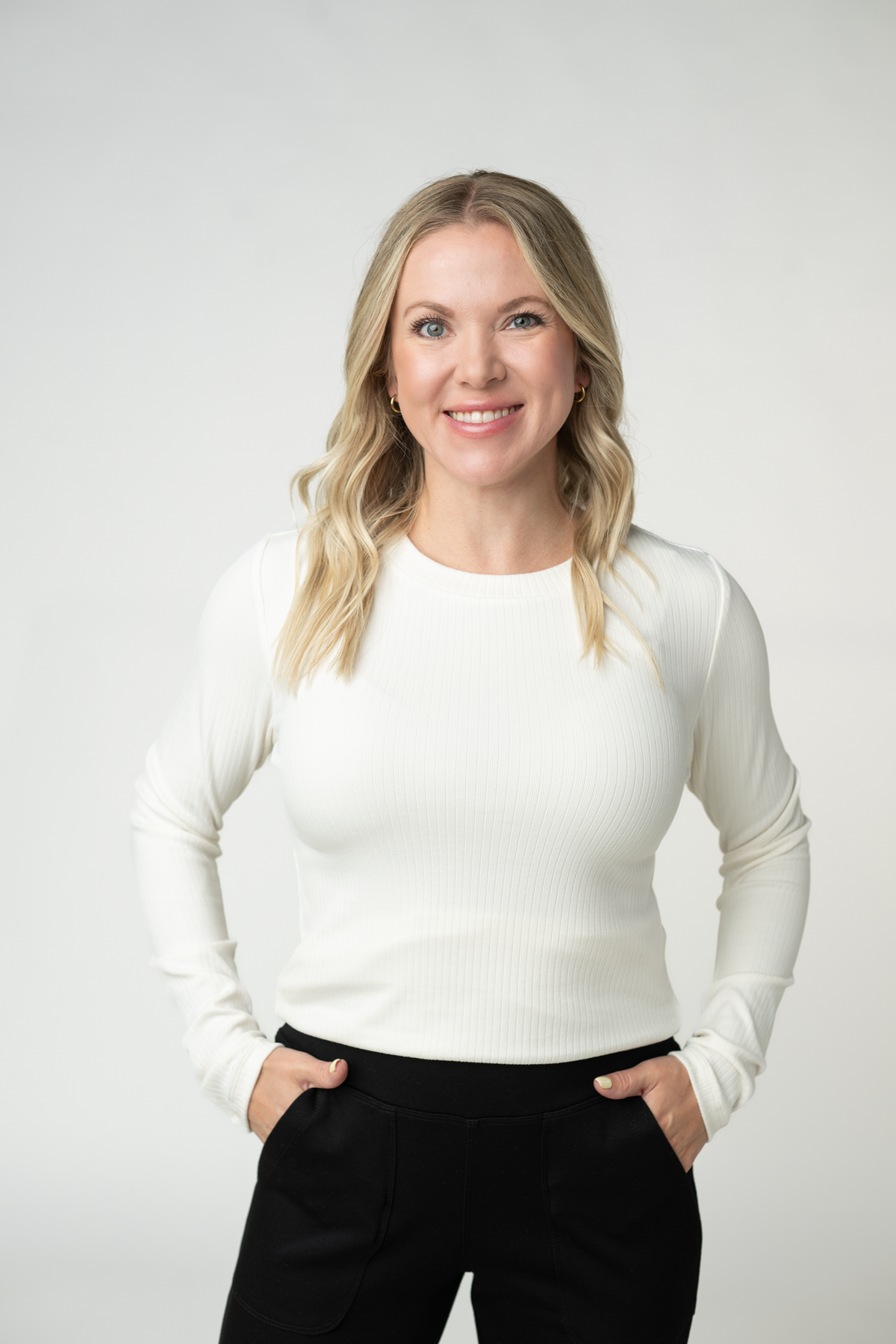 Woman wearing a white long-sleeve top and black pants against a plain background